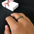Anillo tejido ajustable de Magillas con cuentas doradas sobre cordón negro.