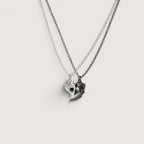 Magillas collares para parejas en forma de corazón, uno plateado y otro negro, elaborados en rodio con proyección "te amo" en 100 idiomas.