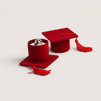 Magillas estuche de terciopelo rojo con forma de birrete de graduación, con borla roja y anillo dorado en el interior.