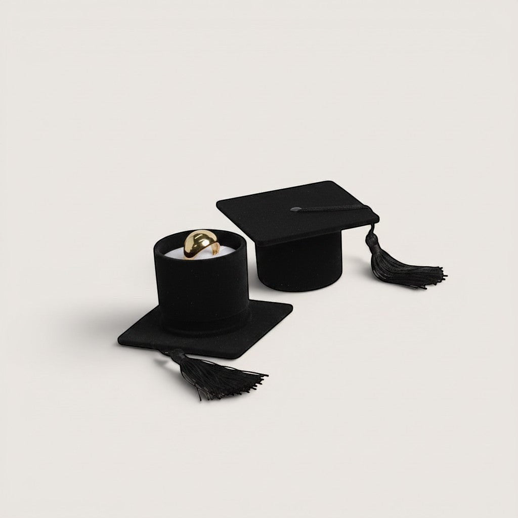 Estuche de terciopelo rojo con forma de birrete de graduación, con borla roja y un anillo dorado en su interior. Magillas.