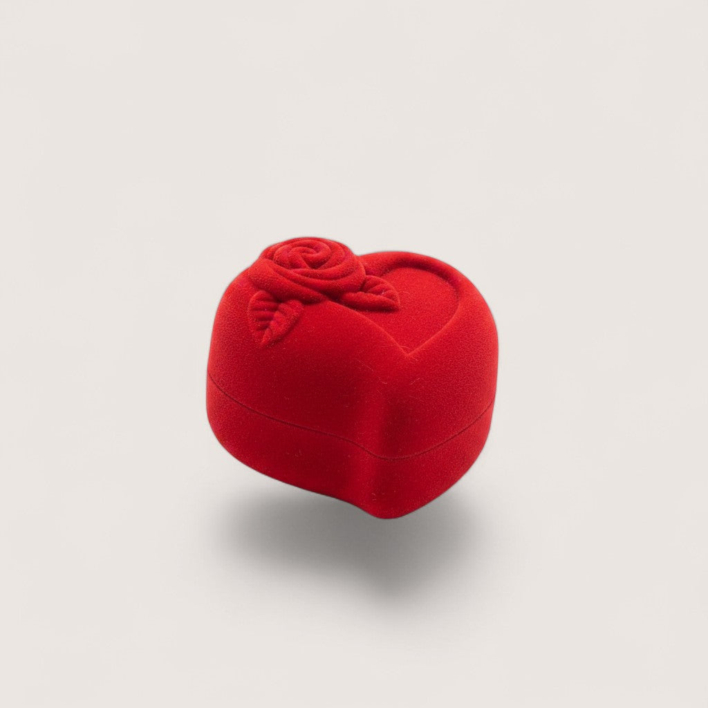 Magillas estuche de terciopelo rojo en forma de corazón con rosa en relieve, sostenido en una mano.
