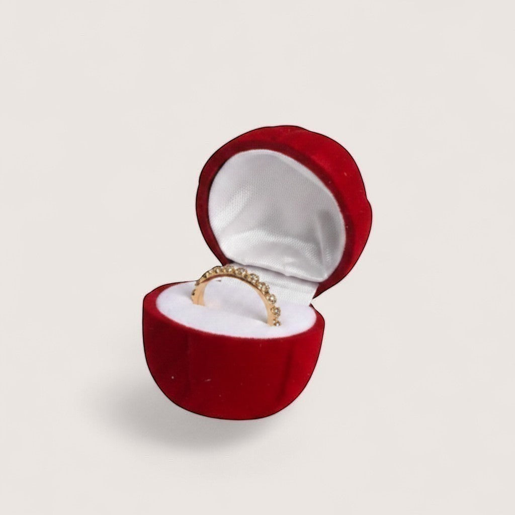 Estuche de terciopelo rojo en forma de rosa con anillo de diamantes, sostenido por una mano con uñas pintadas de azul claro.