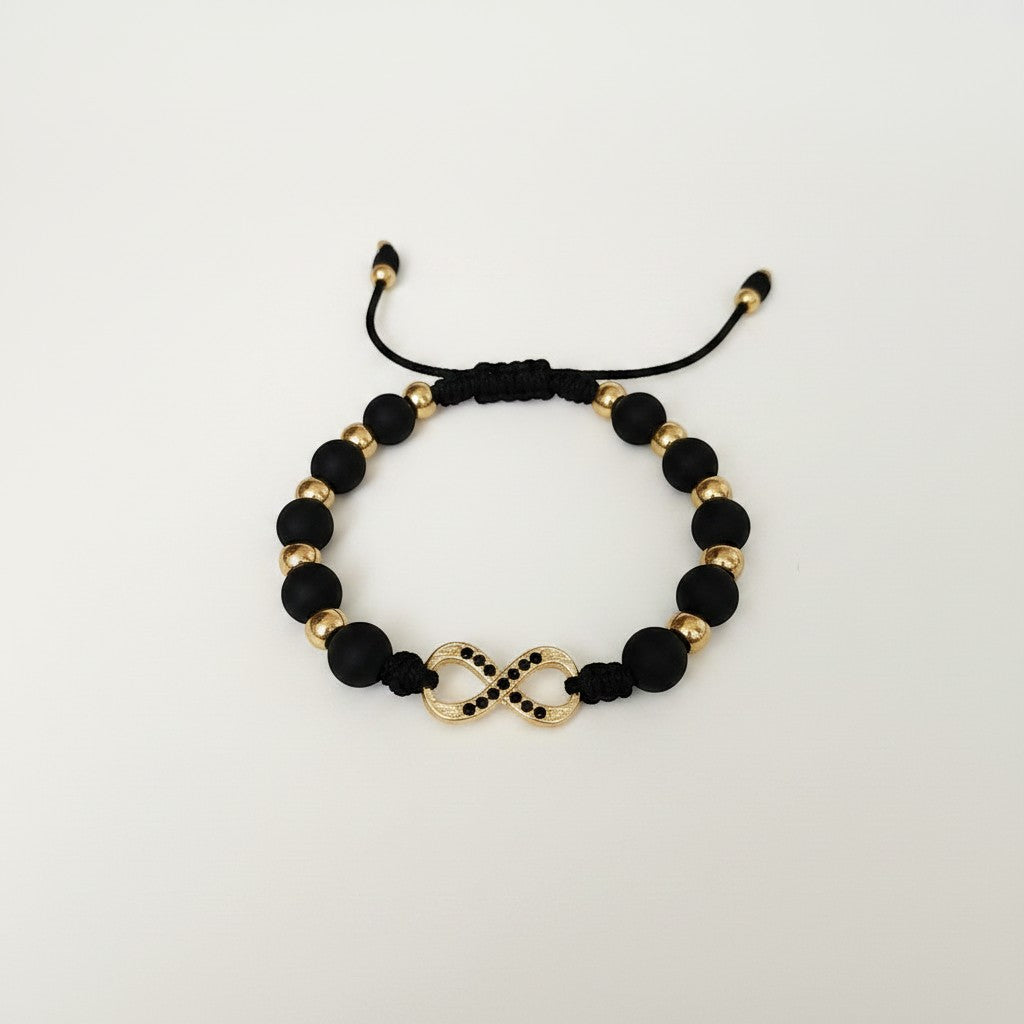 Magillas black beaded bracelet with gold infinity symbol and black rhinestones, made of stainless steel, rhodium, and neoprene.