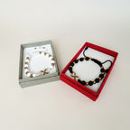 Magillas Pulsera Amor Infinito set featuring black and white beaded bracelets with gold infinity charms in gift boxes