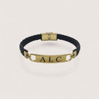Pulsera esclava de cuero trenzado negro con placa personalizable de acero inoxidable y cierre dorado.
