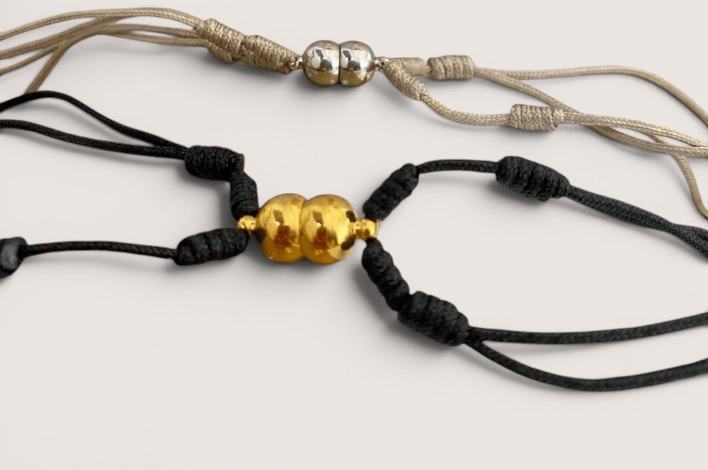 Pulsera de acero inoxidable Magillas con imán, disponible en negro y beige, con cuentas doradas y plateadas.