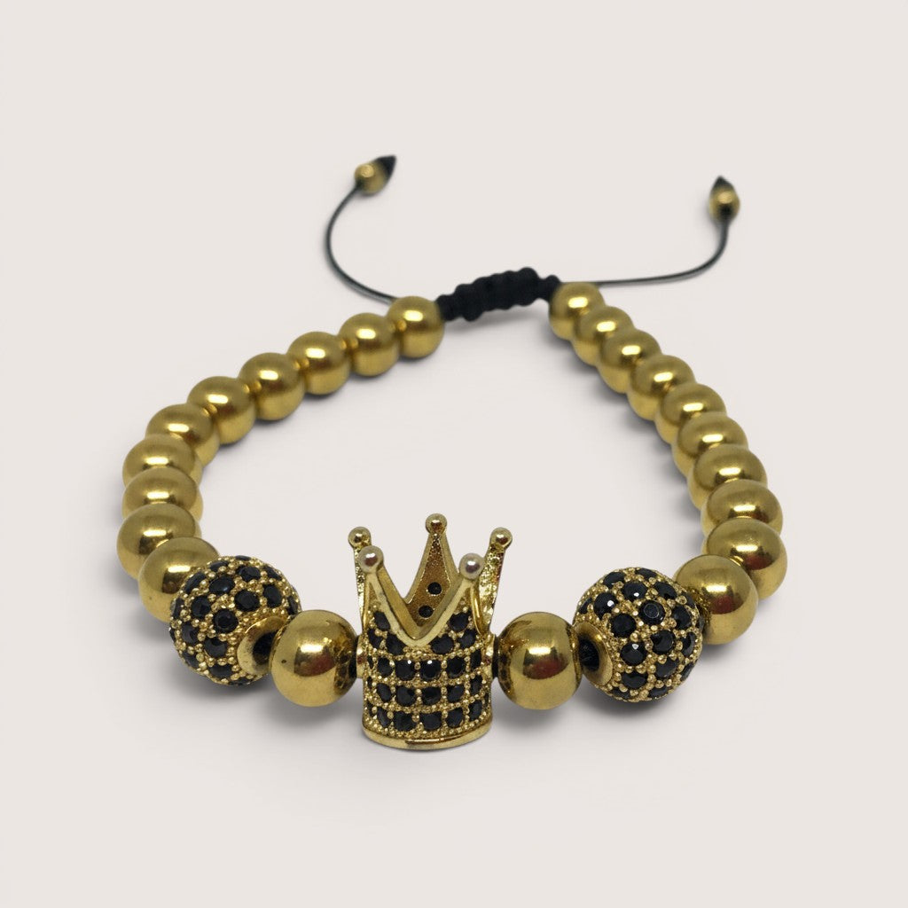 Pulsera Magillas de acero inoxidable y rodio con cuentas doradas, corona central y detalles de circonitas negras.