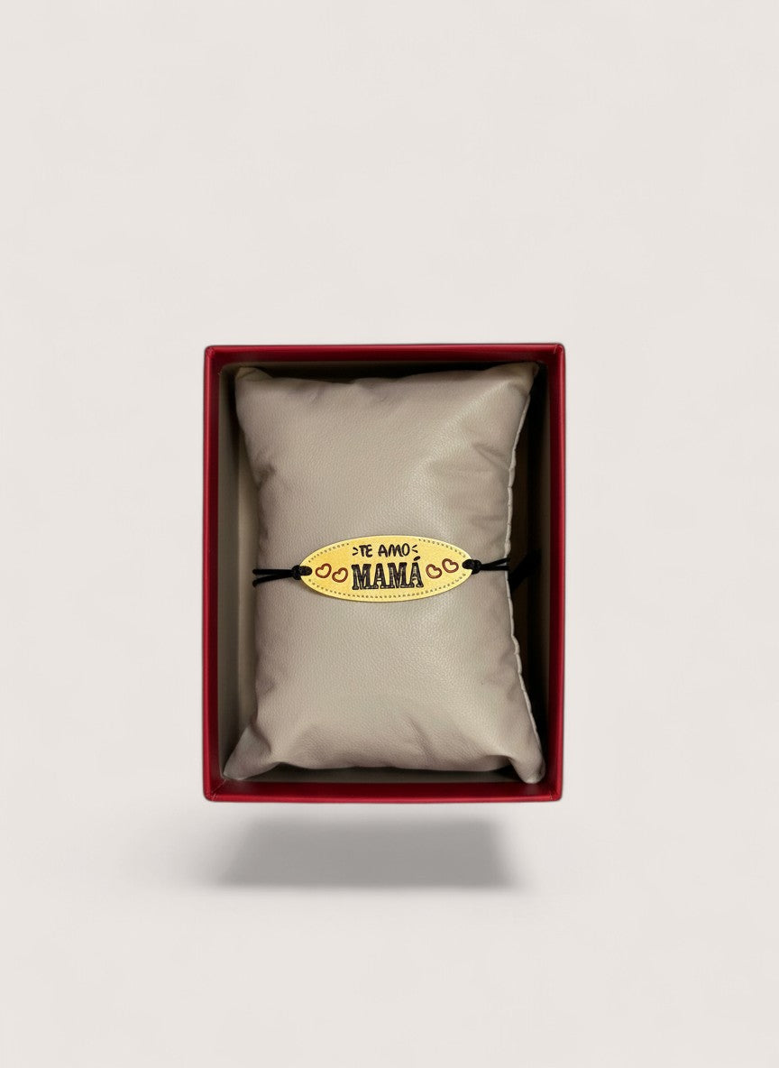 Pulsera Magillas "Te Amo Mamá" con dije ovalado dorado y cordón negro ajustable, adornada con corazones.