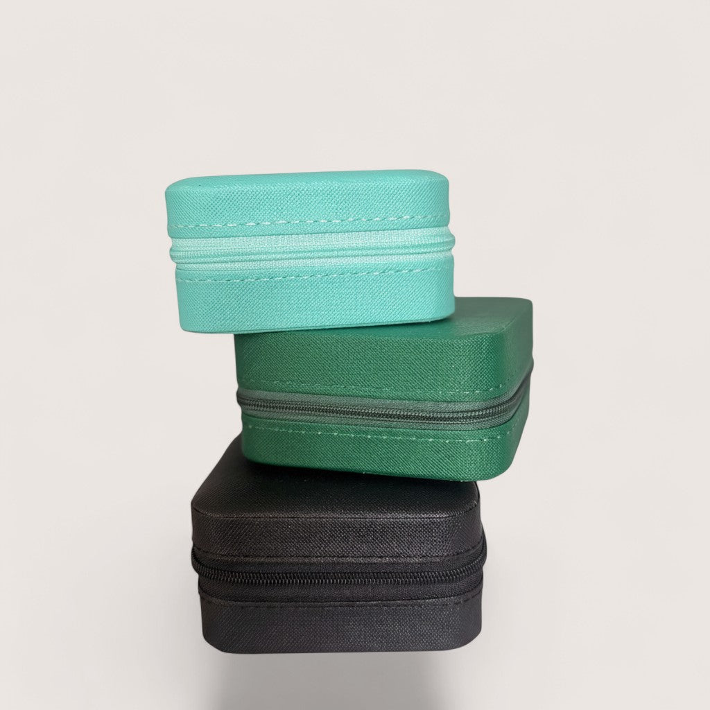 Magillas portable travel jewelry cases stacked in mint green, forest green, and black with secure zipper closures.